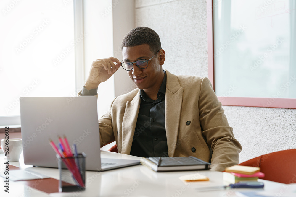 Obraz premium Busy african businessman in glasses working on laptop while sitting in modern coworking