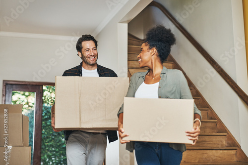 Couple homeowners moving in, carrying boxes and unpacking in new purchased home as real estate investors. Smiling, happy and cheerful interracial man and woman, first time buyers and property owners photo