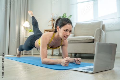 Asian woman wearing sportswear exercising at home.Sport young female doing yoga plank and watching online tutorial on laptop in living room.Healthy lifestyle concept.