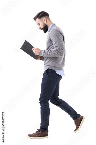 Profile view of young bearded businessman walking while reading notebook or planner. Full body isolated on transparent background. photo