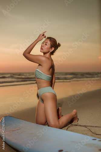 Young woman wearing  bikini sitting beside the surf board for sup surfing on the beach at the sea on sunset of day,holliday summer vacation concept,shilouete photo, photo