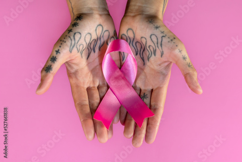 Manos de mujer con tatuajes sosteniendo lazo rosa de la lucha contra el cáncer de mama.