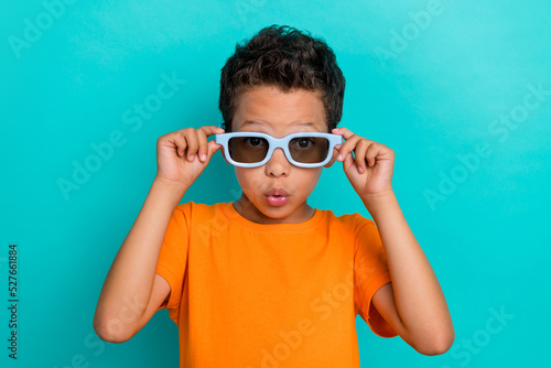Photo of impressed funky small man wear yellow t-shirt arms dark spectacles isolated turquoise color background