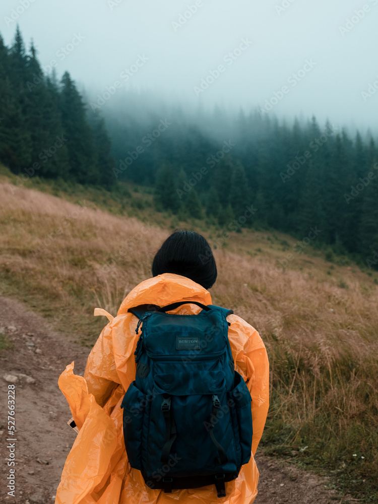 a lonely traveler in the mountains is walking with a backpack in a yellow raincoat in foggy weather a lonely traveler in the mountains is walking with a backpack in a yellow raincoat in foggy weather
