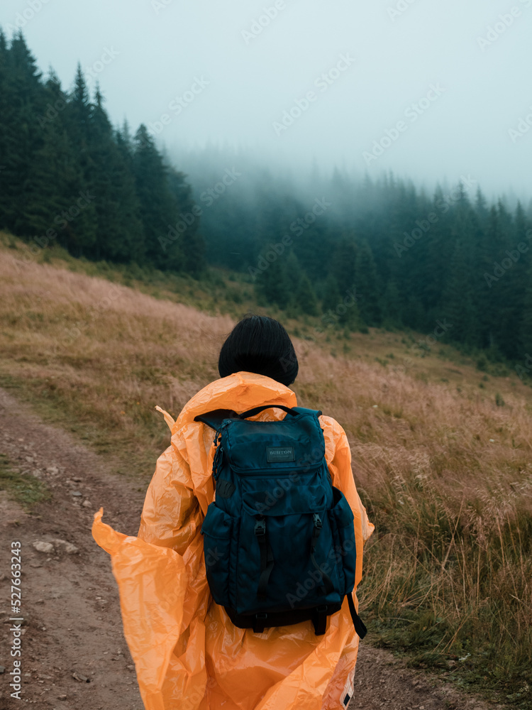 a lonely traveler in the mountains is walking with a backpack in a yellow raincoat in foggy weather a lonely traveler in the mountains is walking with a backpack in a yellow raincoat in foggy weather