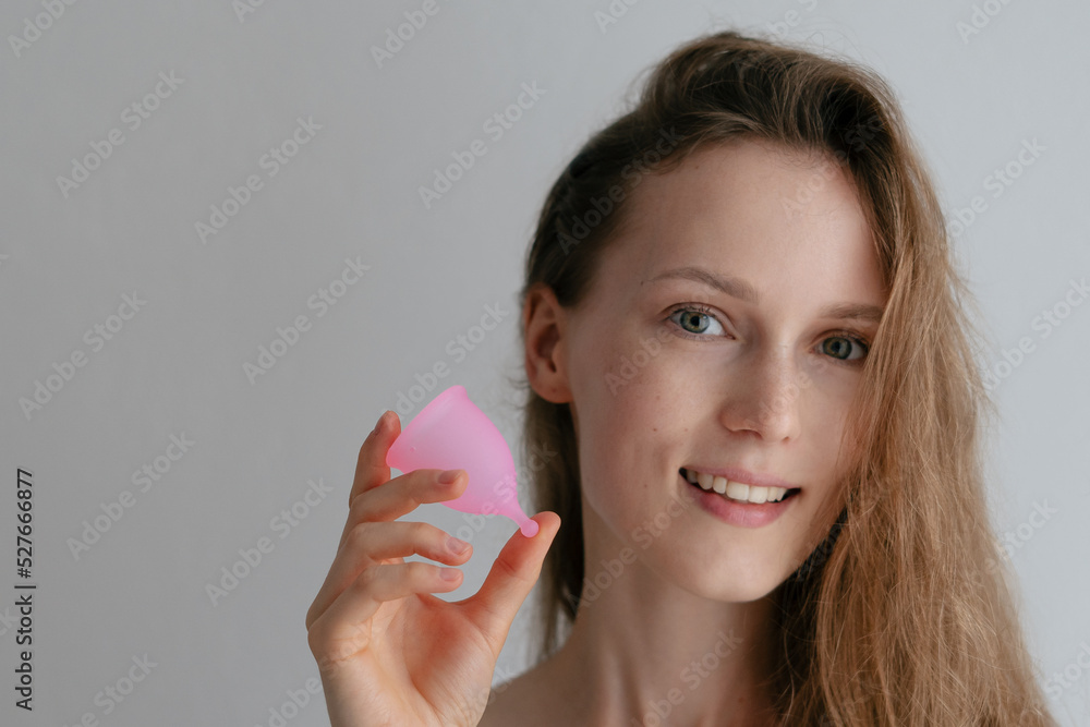 Portrait of an attractive woman holding a pink menstrual cup. Silicone alternative to tampons and pads in period. Reusable hygiene product Portrait of an attractive woman holding a pink menstrual cup. Silicone alternative to tampons and pads in period. Reusable hygiene product