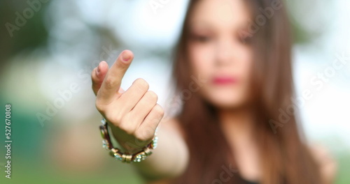 Girl in 20s gesturing with hand and finger to come, inviting viewer
