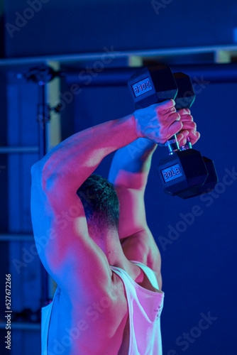 Young man training in gym lifting dumbbells with blue and purple lightning