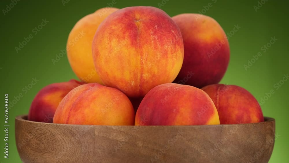 Fresh peaches in wooden bowl, rotation. Juice peach fruits on green background