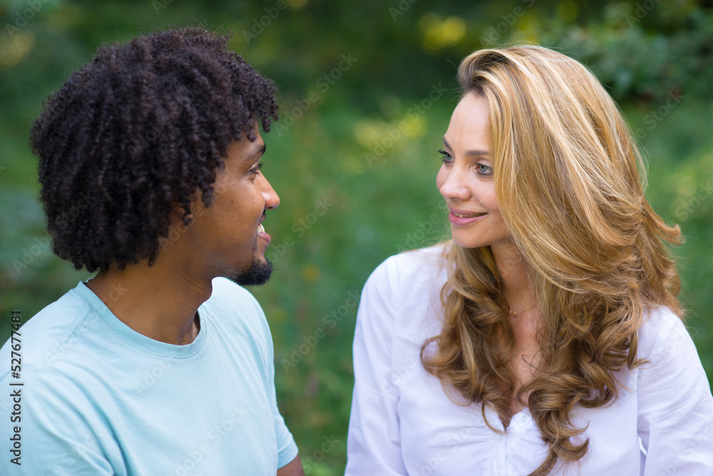 Young mixed race couple talking while sitting in the summer nature Young mixed race couple talking while sitting in the summer nature