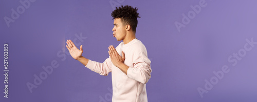 Profile portrait of young hispanic guy with dreads acting like he is ninja or martial arts fighter, practice his kung-fu or taekwondo skills, standing purple background photo