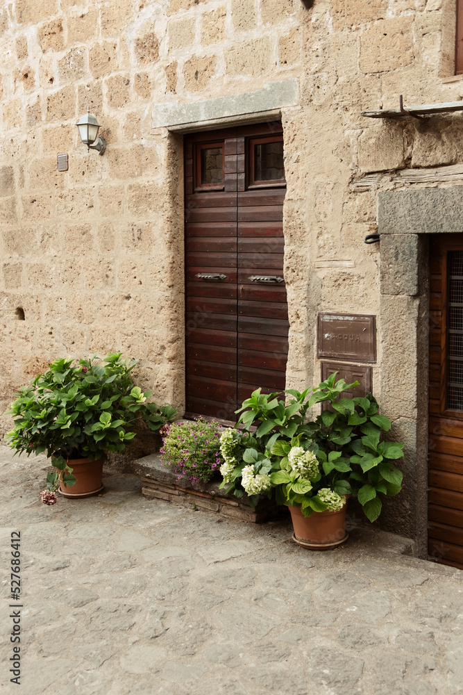 Exterior shot of spectacular ancient buildings of stones with cobblestone courtyard in the foreground and with stone stairway to entrance door decorated with plants in flower pots and plants,