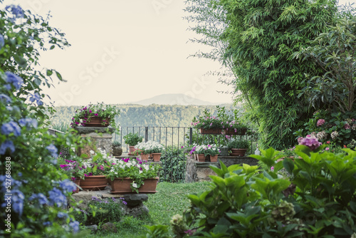 Exterior shot of beautiful garden, scenic mountain gorge with green forest , a lot of pots with blooming flowers, hedonic leisure, place for wonderful rest, background for quotes, place for your text