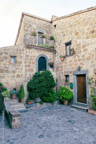 Exterior shot of spectacular ancient buildings of stones with cobblestone courtyard in the foreground and with stone stairway to entrance door decorated with plants in flower pots and climbing plants,