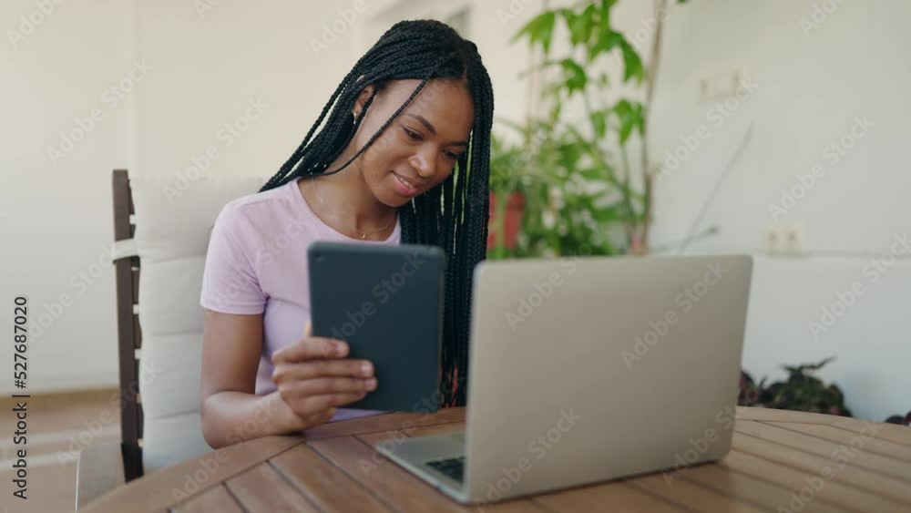 African american woman using laptop and touchpad sitting on table at home terrace African american woman using laptop and touchpad sitting on table at home terrace
