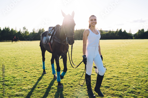 Cheerful horsewoman walking on field with horse photo