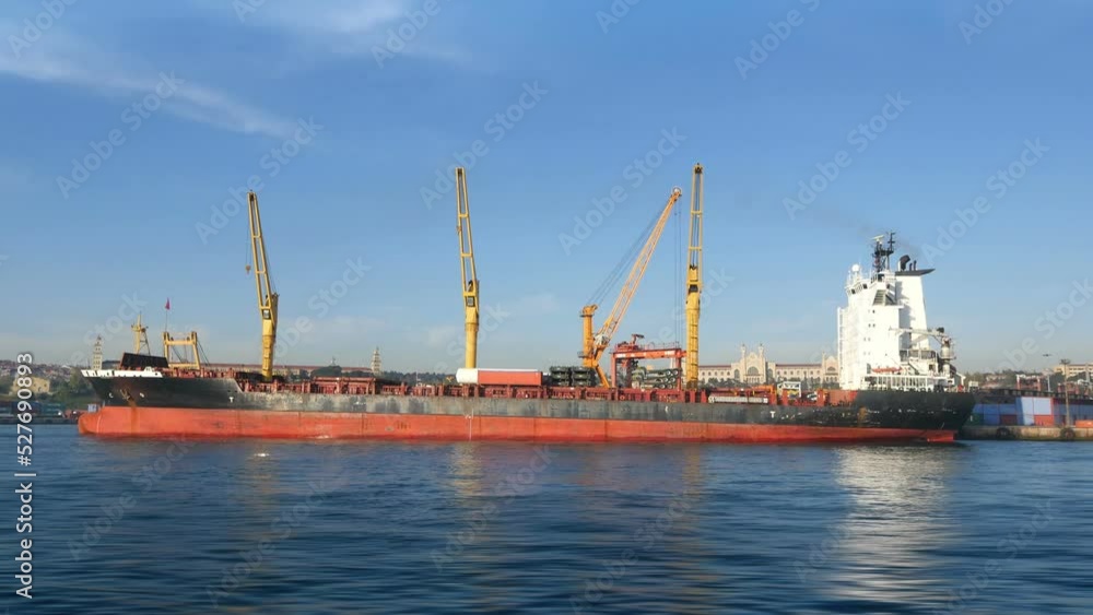 Pan shot of cargo container ship berthed in commercial sea port. A video featuring a pan from the waterside of an industrial seaport including cargo ship with containers, port cranes and operational a Pan shot of cargo container ship berthed in commercial sea port. A video featuring a pan from the waterside of an industrial seaport including cargo ship with containers, port cranes and operational a