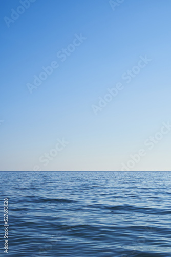 Dark blue water from the sea with blue sky. Light comes from the right. Vertical format, also suitable as a poster or background. Free space for text or objects. 
