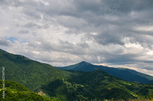 Beautiful summer landscape with forested hills, mount Strymba in the distance, and sky with low clouds. Carpathian mountains, Ukraine