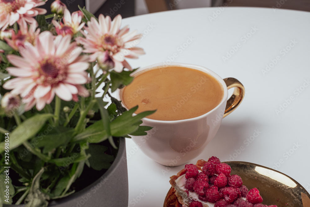 View to blurred white cup with delicious coffee on white background. Beautiful pink chrysanthemums in pot in the foreground. Place for your text. View to blurred white cup with delicious coffee on white background. Beautiful pink chrysanthemums in pot in the foreground. Place for your text.
