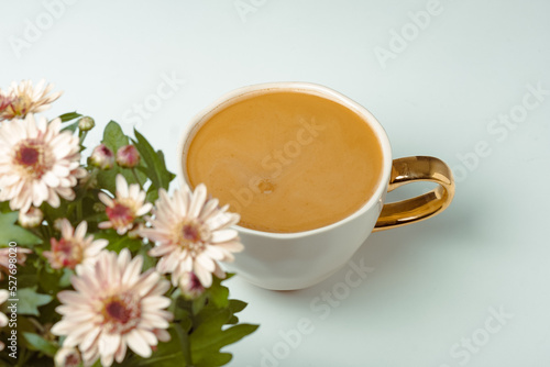 View to blurred white cup with delicious coffee on white background. Beautiful pink chrysanthemums in pot in the foreground. Place for your text. glamor lifestyle, hedonic holidays, coffee lover
