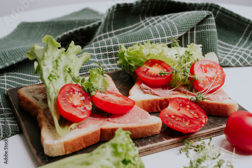 Close-up of delicious toasts decorated with microgreens and tomatoes and fresh lettuce. Healthy breakfast. Green towel in background. White background. 