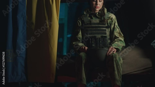 Ukrainian female soldier in a dugout with a Ukrainian flag puts on a helmet in anticipation of an attack by Russian invaders - Ukrainian war concept.  photo