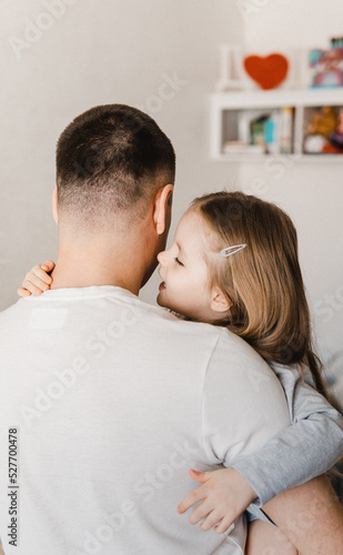 Portrait of father holding daughter on his arms. Girl cuddling father and telling him a secret. Daughter kiss her father. Selective focus. Film grain