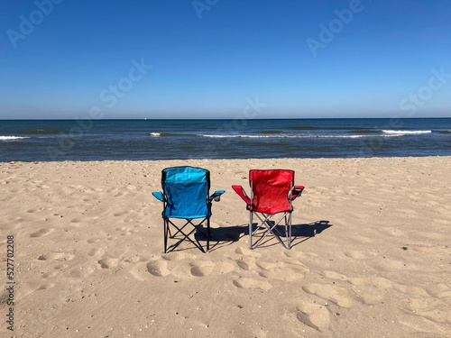 Fototapeta Naklejka Na Ścianę i Meble -  A blue and a red chair standing empty on the beach of the North Sea under a blue sky