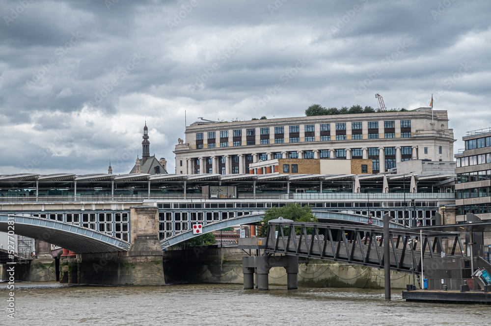 London, England, UK - July 6, 2022: From Thames River. Blackfriars railway bridge landing on north shore under heavy cloudscape. Buildings peep above.