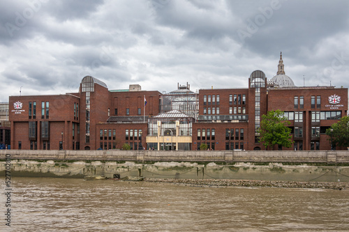 London, England, UK - July 6, 2022: From Thames River. red brick modern City of London School building under heavy cloudscape. Dome of St. Paul's Cathedral in back.