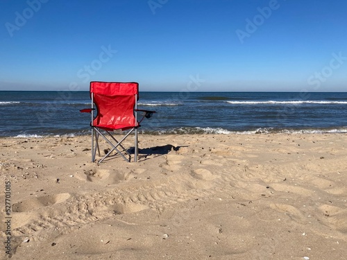 A red chair standing empty on the beach of the North Sea under a blue sky © Marcus