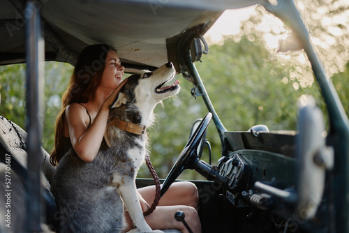 A beautiful young woman sits behind the wheel of her car together with a husky breed dog and smiles cheerfully enjoys the journey
