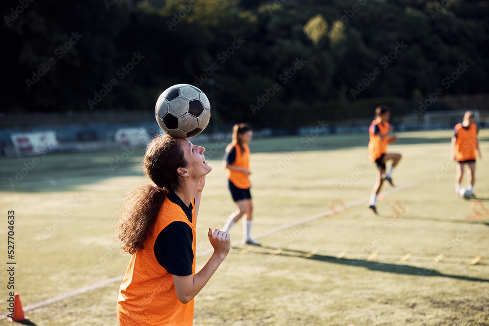 Happy player balancing soccer ball on her head during sports training.