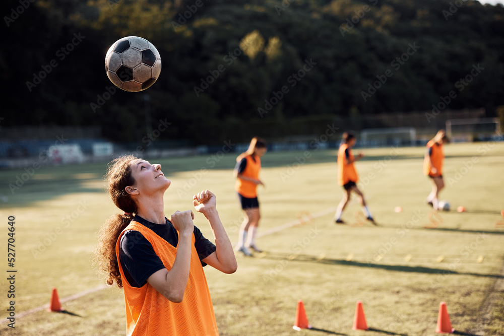 Smiling female soccer player heading the ball during practice on playing field.