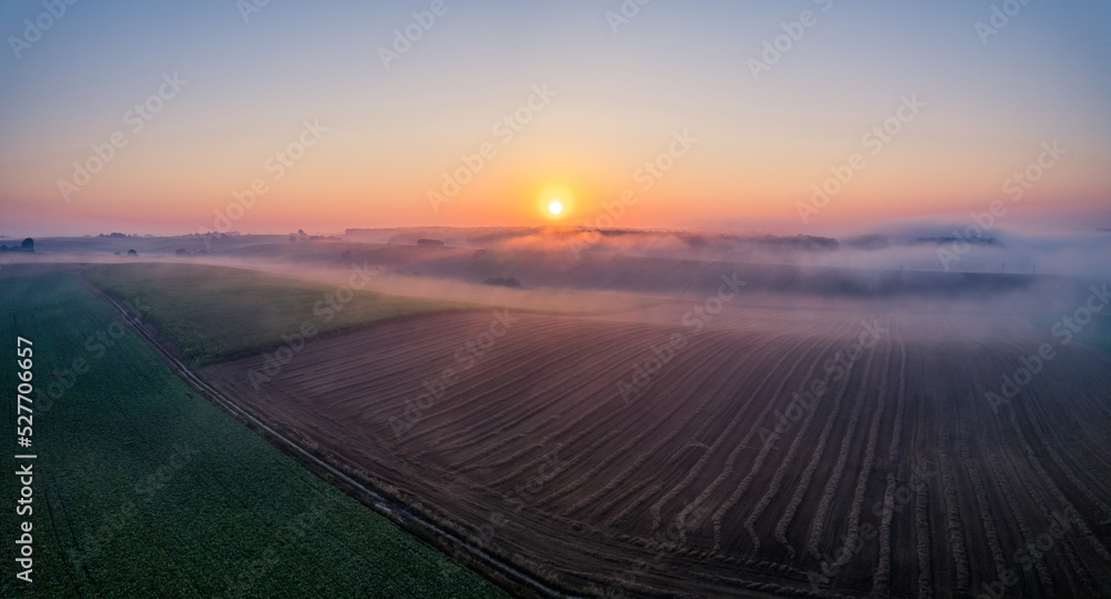 Birdseye view of vibrant orange sunrise over green and brown farm fields with morning fog in Roztocze Poland. Wide horizontal shot. High quality photo