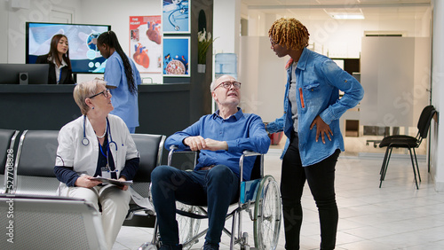 Photos Man with physical impairment attending medical checkup with doctor and caretaker in waiting area