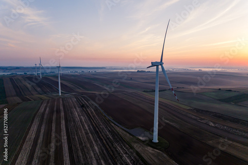 Wind turbines standing in colorful fields at sunrise. Foggy horizon. Renewable energy. Ecology. Horizontal shot . High quality photo © PoppyPix