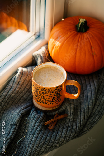 Cup of coffee decorated Halloween pumpkins on knitted woolen plaid with orange pumpkin and cinnamon sticks. Cozy home autumn decor, hygge style.