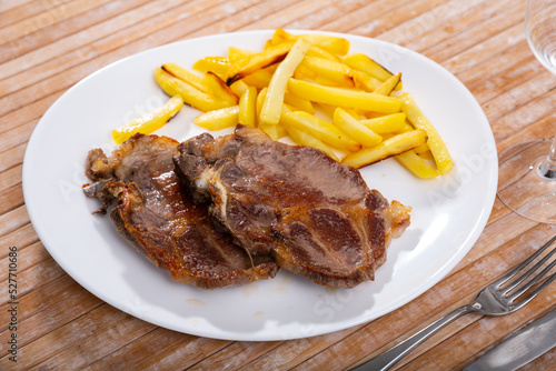 Appetizing roasted bone-in pork chop with side dish of crispy french fries