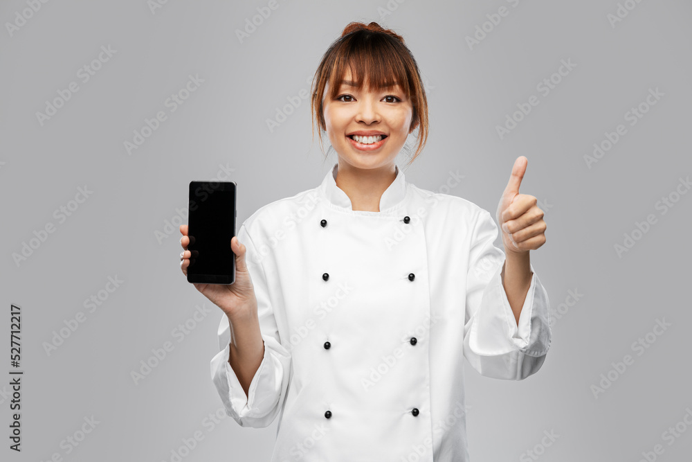 cooking, culinary and people concept - happy smiling female chef in white jacket with smartphone showing thumbs up over grey background cooking, culinary and people concept - happy smiling female chef in white jacket with smartphone showing thumbs up over grey background