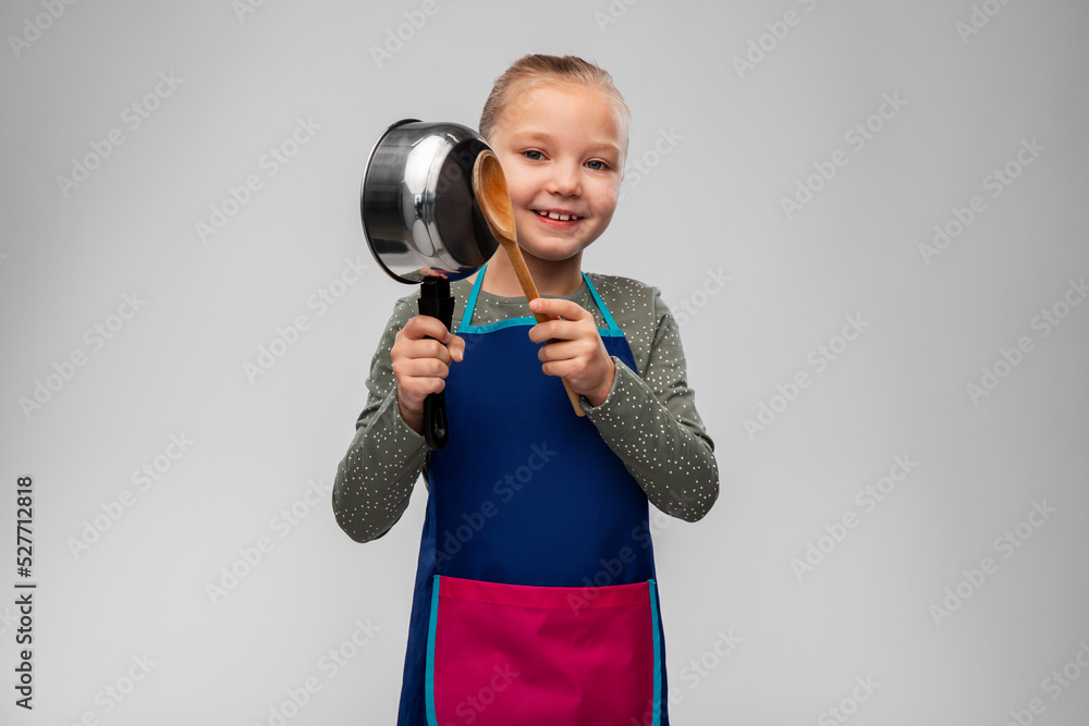 cooking, culinary and profession concept - happy smiling little girl in apron playing with saucepan and wooden spoon over grey background cooking, culinary and profession concept - happy smiling little girl in apron playing with saucepan and wooden spoon over grey background