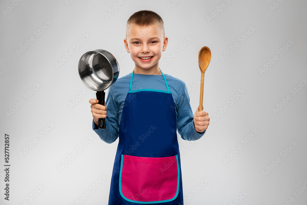 culinary and profession concept - happy smiling little boy in apron with saucepan and wooden spoon cooking food over grey background culinary and profession concept - happy smiling little boy in apron with saucepan and wooden spoon cooking food over grey background