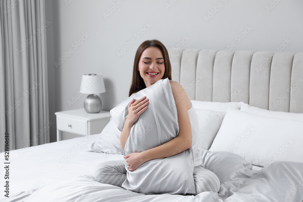Young woman hugging pillow on comfortable bed with silky linens Young woman hugging pillow on comfortable bed with silky linens