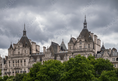 London, England, UK - July 6, 2022: From Thames River. 2 Whitehall towers behind green folliage belt under gray cloudscape.