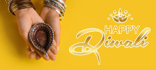 Female hands with diya lamp on yellow background. Celebration of Indian holiday Diwali (Festival of lights)