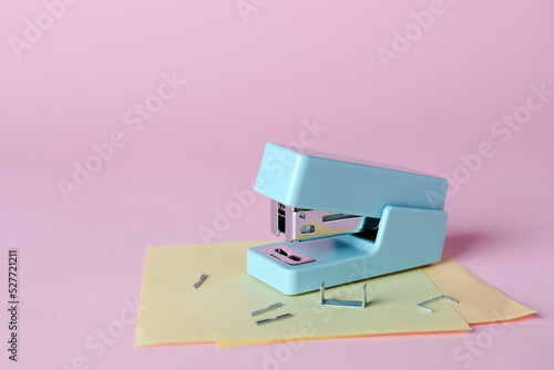 Stapler with sticky notes and staples on pink background