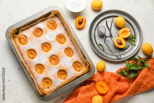 Baking tray with tasty apricot pie and fresh fruits on light table