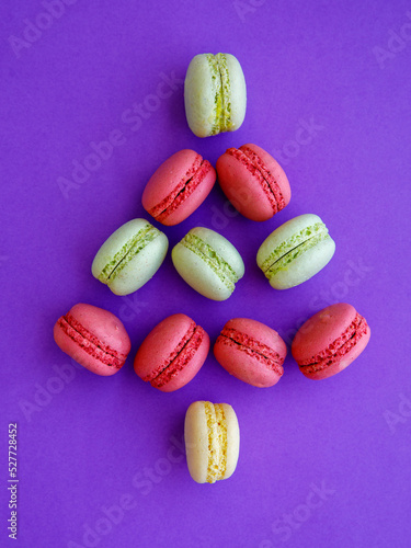 French mint pistachio green tea and red strawberry raspberry macarons shaped as Christmas tree on purple background. Top view flat lay, copy spase, vertical