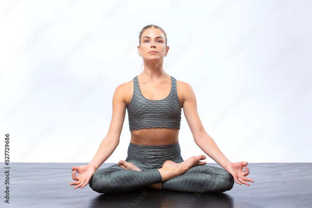 Young woman seated in lotus position against white background.